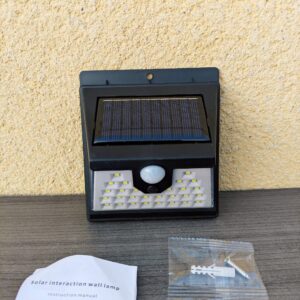 Imagen principal de la lampara de induccion solar led 40 smd raptor r-o423 exterior de frente junto a su manual de instrucciones y kit de tornillos de montaje