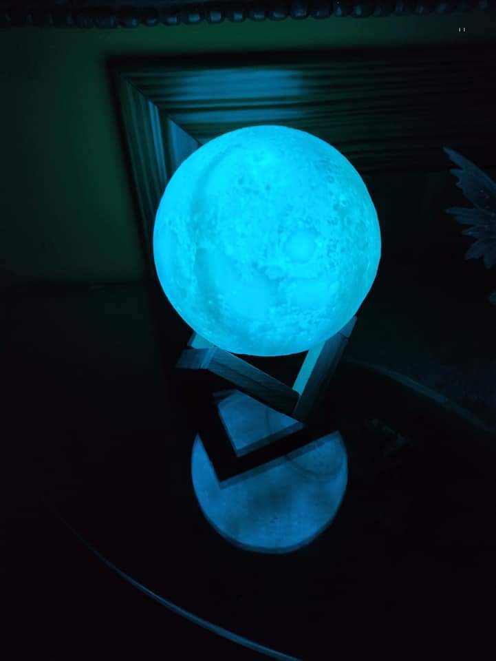 Lámpara Luna 3D Iluminación Azul 🔵 Fotografia real de la lampara luna 3d led 7 colores encendida en la oscuridad emitiendo un tono azul cian brillante sobre su base de madera
