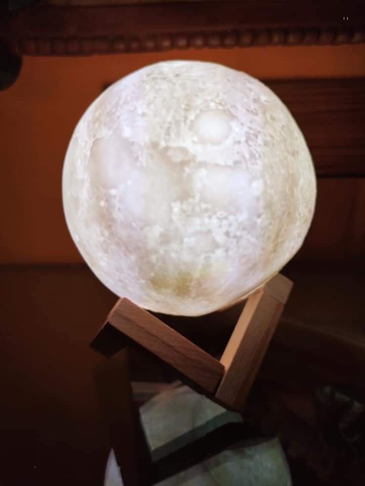Lámpara Luna 3D Iluminación Cálida 🌙 Fotografia real en primer plano de la lampara luna 3d led 7 colores encendida con luz blanca calida sobre su base de madera de tres piezas entrelazadas