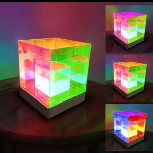 Lampara de mesa cubo rgb con iluminacion multicolor sobre una base de madera mostrando diferentes variaciones de color rosa verde y azul en el lateral